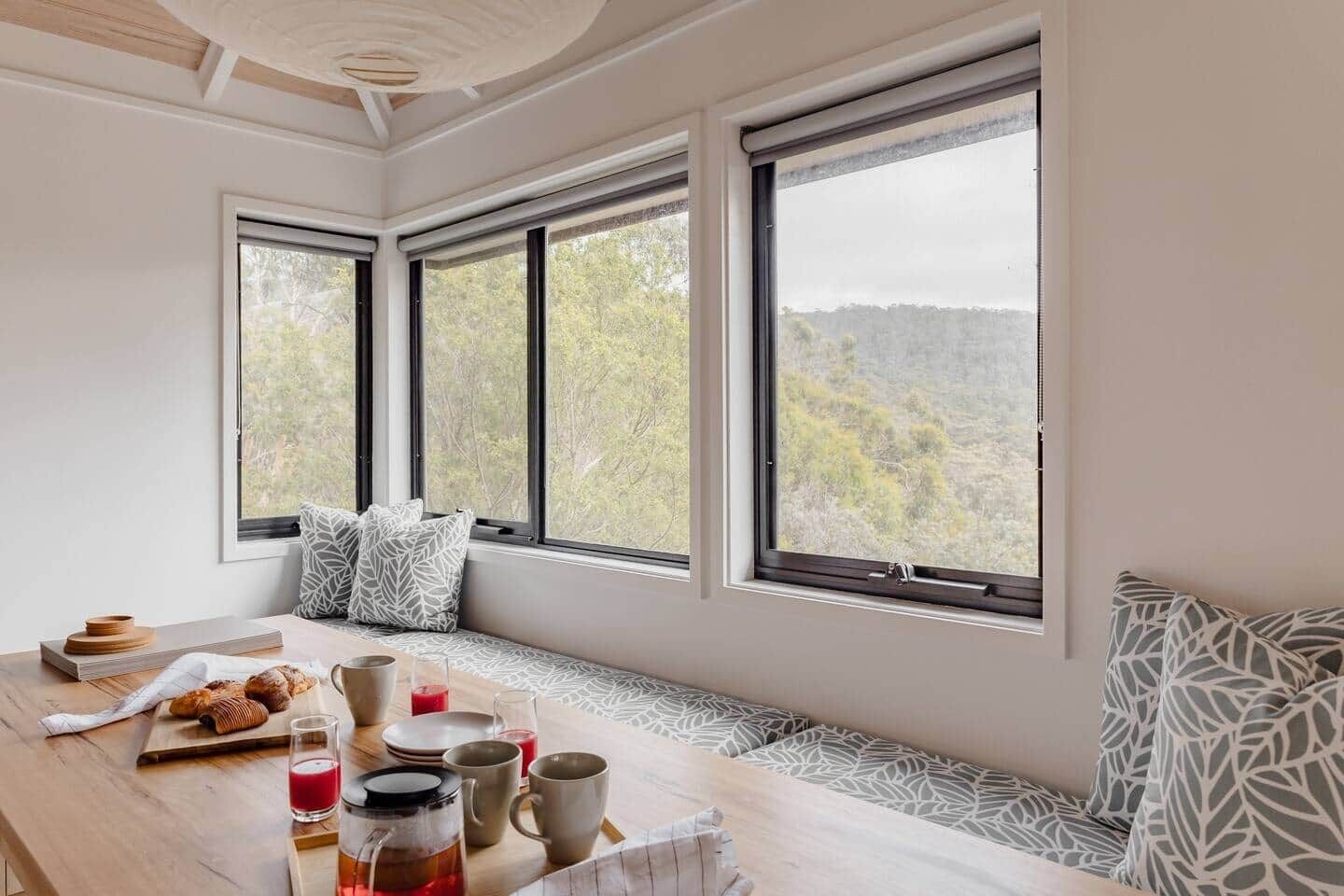 A breakfast setup with a table, seating, and large windows offering a view of trees and hills.