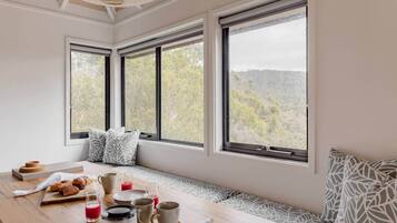 A breakfast setup with a table, seating, and large windows offering a view of trees and hills.