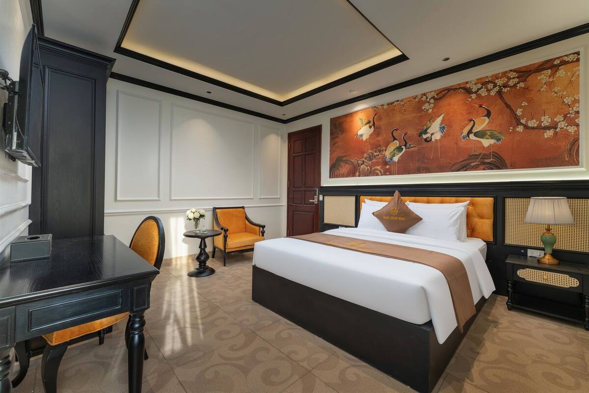 Habitación de hotel con una cama grande, un escritorio, dos sillas, una mesita y un cuadro en la pared.