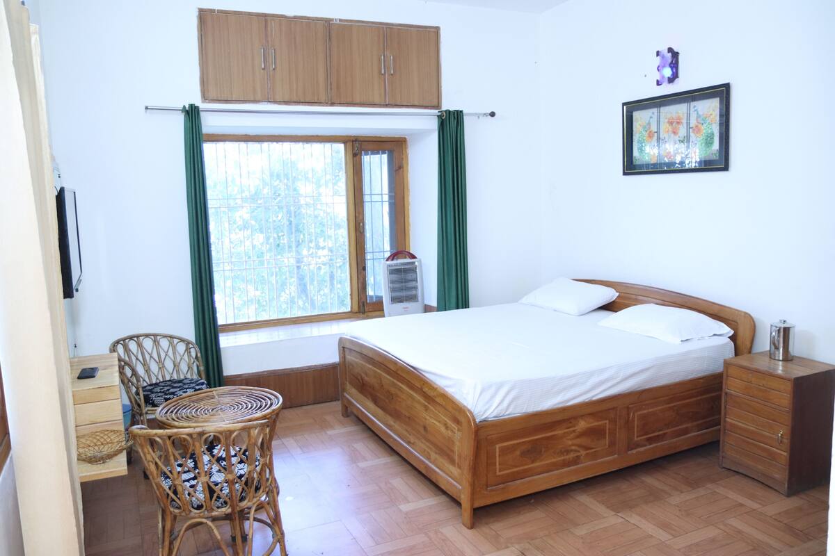 A bedroom with a wooden bed, a chair, a bedside table, and a window with curtains.