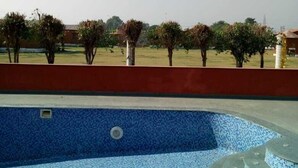 Une piscine aux carreaux de mosaïque bleus, entourée d’un mur rouge et d’arbres.