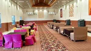 Une salle de conférence dotée de plusieurs tables et chaises, d’un tapis à motifs et d’un plafond en bois avec des luminaires encastrés.