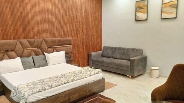 Une chambre avec un grand lit, un canapé gris et un mur d’accent en bois.