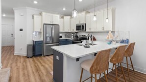 Uma cozinha moderna com armários brancos, eletrodomésticos de aço inoxidável, uma ilha central com banquetas e iluminação pendente.