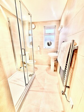 Ein Badezimmer mit Duschkabine aus Glas, Toilette, Waschbecken und Handtuchhalter.