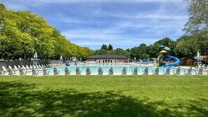 Una piscina con sillas de descanso, un tobogán y un edificio al fondo.