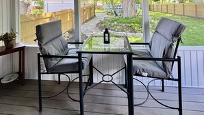 Un patio techado con una mesa y sillas, un ventilador de techo y vista a un jardín trasero.