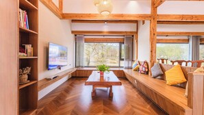 A modern living room with a wooden floor, a central table, a TV on the wall, and large windows with curtains. - Li River Craftsman Village  Guilin (Guilin)
