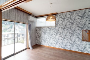 Una habitación con un amplio ventanal corredera que da a un balcón, un papel tapiz estampado, un colgador de techo y un techo de madera.