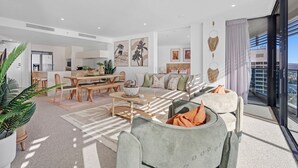 A modern living room with a dining area, a kitchen, and a balcony with a city view. - Oracle Resort Lvl 22 Beach Views (Broadbeach)