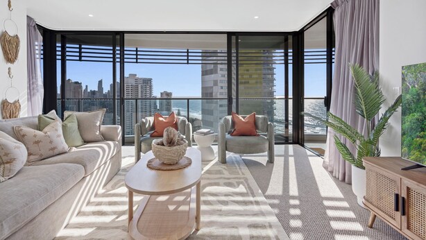 A modern living room with a city view, a sofa, armchairs, a coffee table, and a large window. - Oracle Resort Lvl 22 Beach Views (Broadbeach)