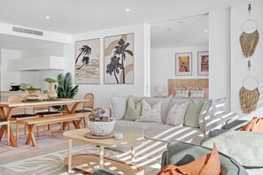 Ein modernes Wohnzimmer mit Sofa, Couchtisch und Essbereich. An den Wänden befinden sich gerahmte Kunstwerke und eine dekorative Wandgestaltung.