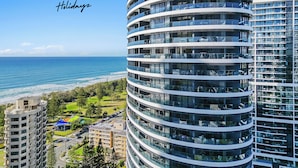A modern, multi-story building with a curved facade, located near a beach with clear blue waters. - Oracle Resort Lvl 22 Beach Views (Broadbeach)
