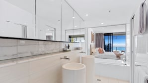 A modern bathroom with a marble countertop, a bathtub, and a large mirror. - Oracle Resort Lvl 22 Beach Views (Broadbeach)
