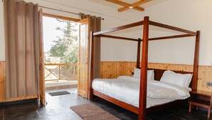 A four-poster bed with white linens, a wooden headboard, and a view of the outdoors through a glass door. - The Meemos Cafe And Cottages (Mussoorie)