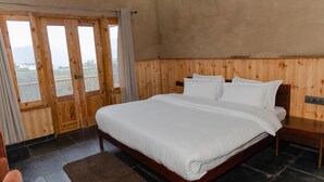A bedroom with a large bed, wooden paneling, a view through a door, and a nightstand. - The Meemos Cafe And Cottages (Mussoorie)