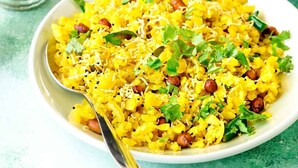 A bowl of yellow rice garnished with herbs and nuts, accompanied by glasses of a brown beverage, likely chai, on a teal surface. - Hotel Royal Inn (Pune)