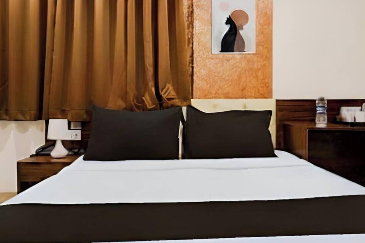 A hotel room with a bed, brown curtains, a nightstand with a lamp, and a framed picture on the wall.