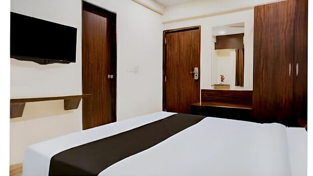 A hotel room with a bed, a TV mounted on the wall, wooden wardrobes, and a mirror. - Hotel Royal Inn (Pune)