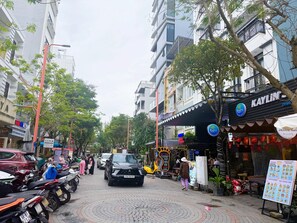 A street with parked motorcycles, a black car, and a building with a sign reading 'Kaylin.' - Sweet Home Hotel & Apartment (Ngu Hanh Son)