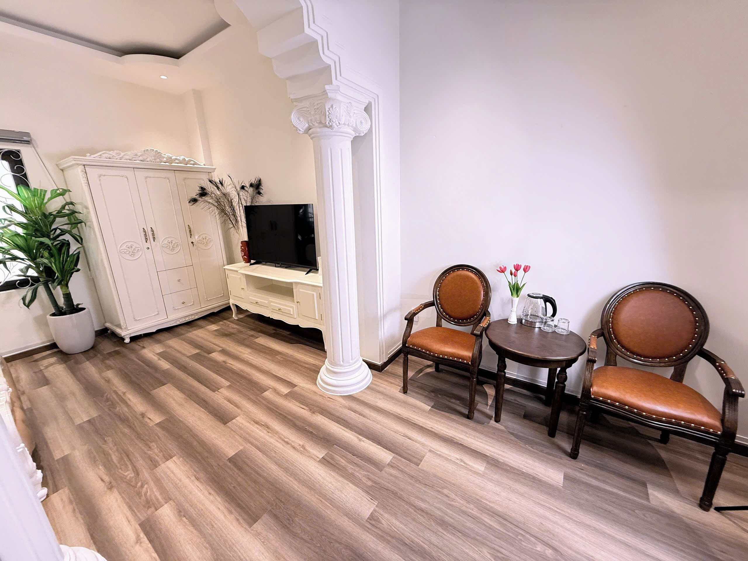 Une pièce avec un plancher en bois, des meubles blancs, une télévision et une plante.