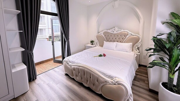 Une chambre avec un grand lit, une armoire, une plante en pot et une vue sur l’extérieur.