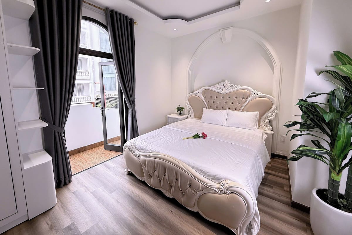 A bedroom with a large bed, a wardrobe, a potted plant, and a view of the outside.