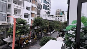 Une vue de rue avec un mélange de bâtiments modernes et traditionnels, un café doté d’une terrasse, et une enseigne d’hôtel bien visible.