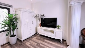 Une pièce avec un meuble blanc, un téléviseur posé sur un meuble blanc, une plante en pot et un plancher en bois.