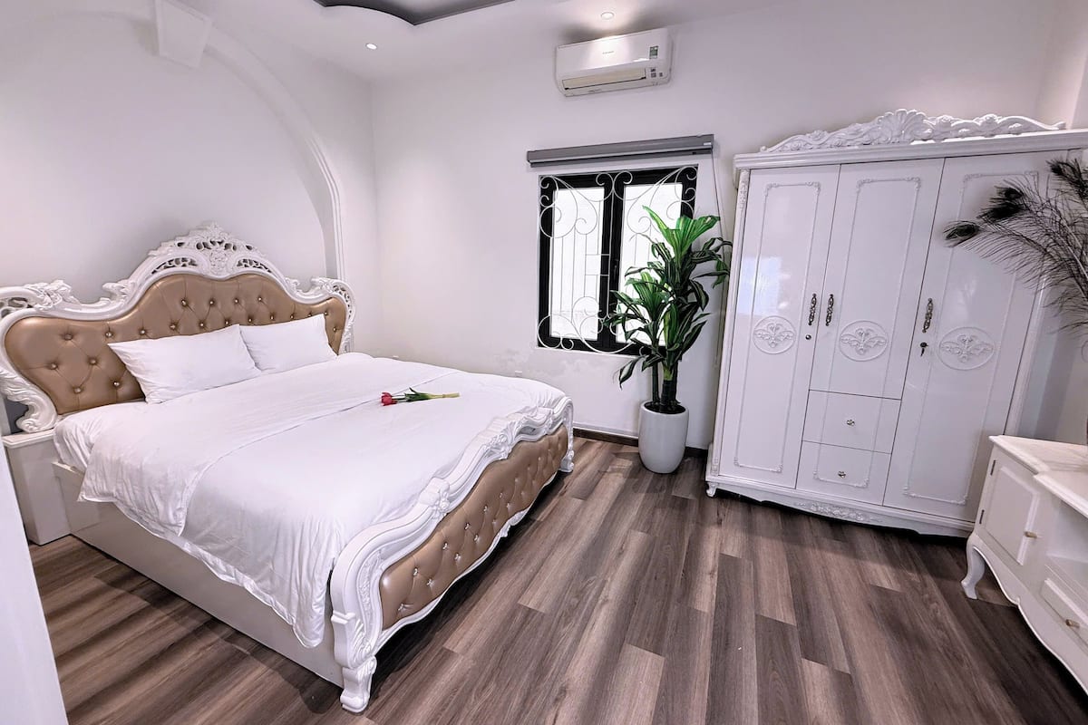 A bedroom with a bed, a wardrobe, a potted plant, and a window.