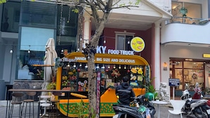 Un camion-restaurant avec une enseigne colorée, un arbre et une moto garés devant.