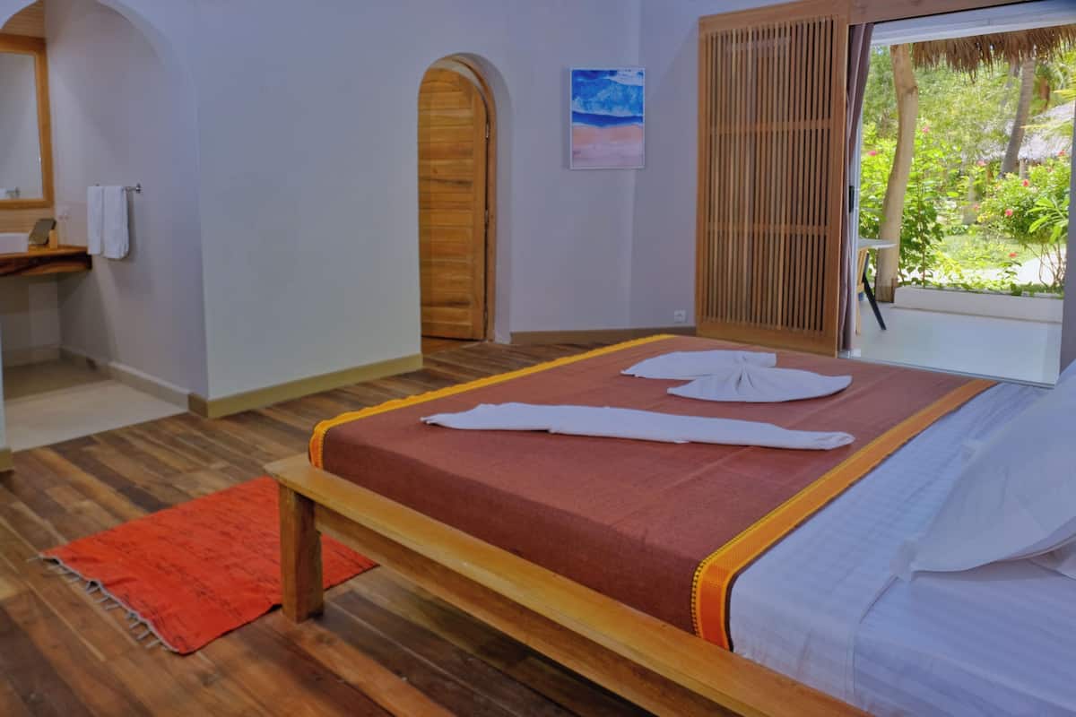 A room with a bed, a wooden door, a window, and a small bathroom area.