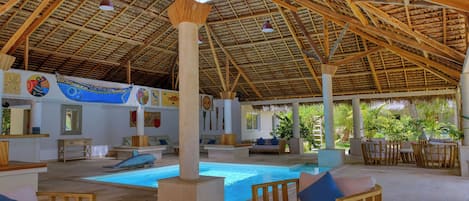 A spacious indoor pool area with wooden beams and columns, surrounded by comfortable seating and a decorative mural.