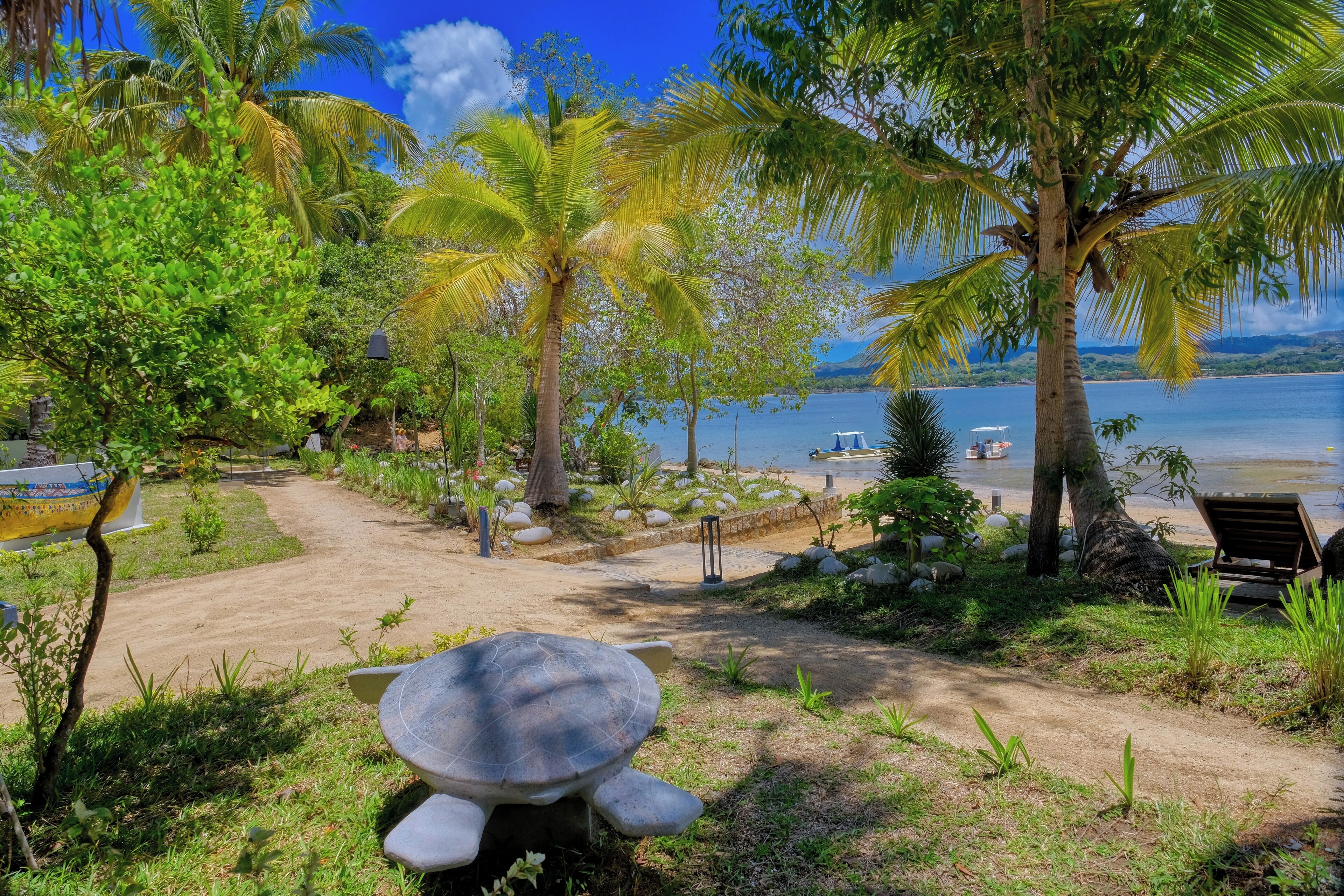 Un jardín tropical con una gran estatua de tortuga, palmeras y vista al mar.