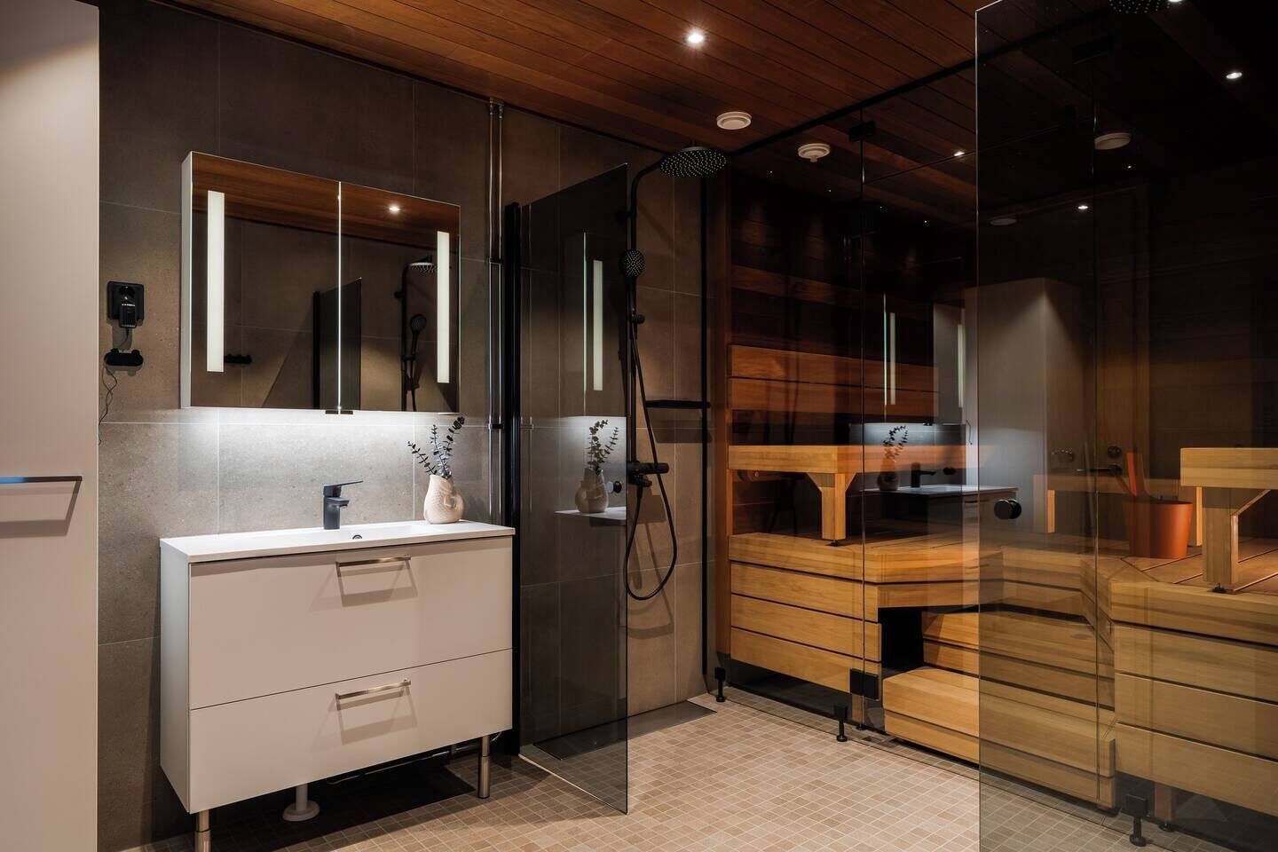 Un baño moderno con cabina de ducha de vidrio, un tocador blanco con espejo, y un tocador de madera con lavabo y espejo.