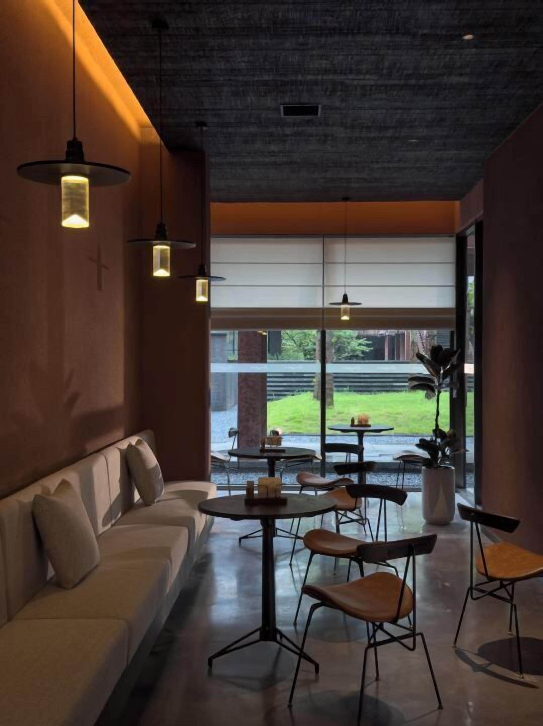 A modern interior with a sofa, tables, chairs, pendant lights, and a view of the outdoors.