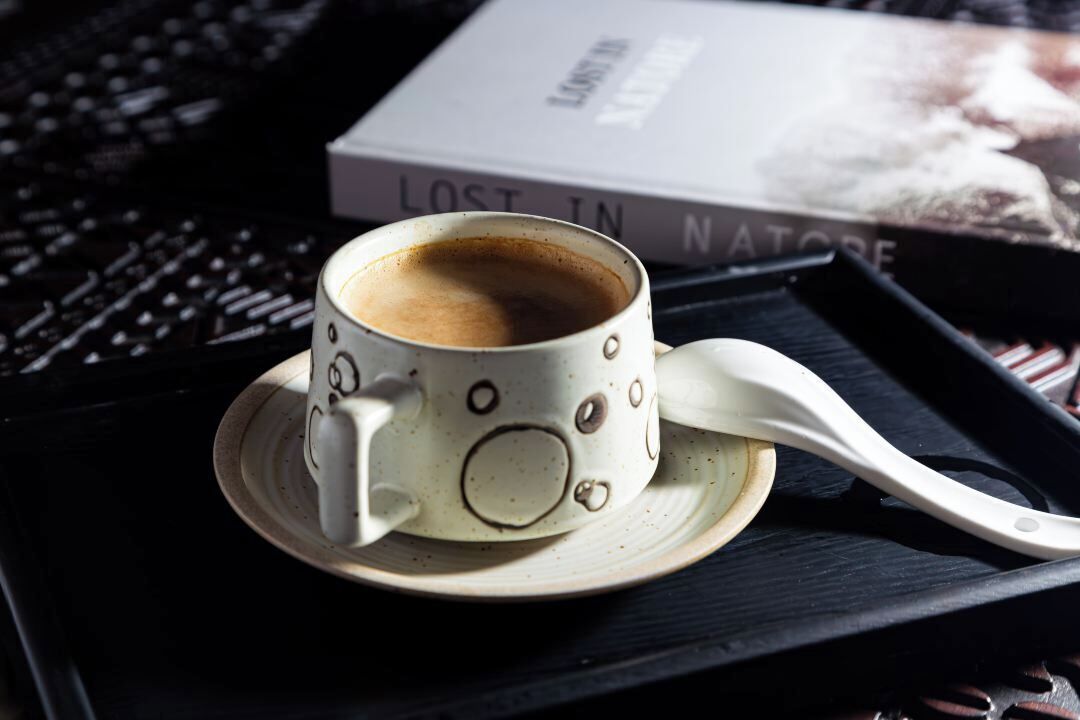 Une tasse de café sur un plateau, avec une cuillère, et en arrière-plan, un livre intitulé « Perdus dans la NATURE ».