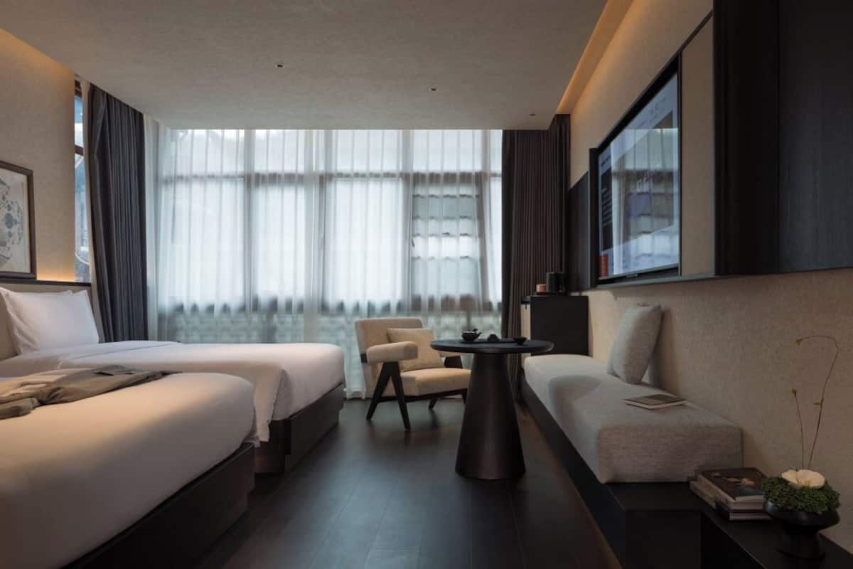 Une chambre d’hôtel moderne avec deux lits, un canapé, une petite table et une grande fenêtre avec des rideaux.