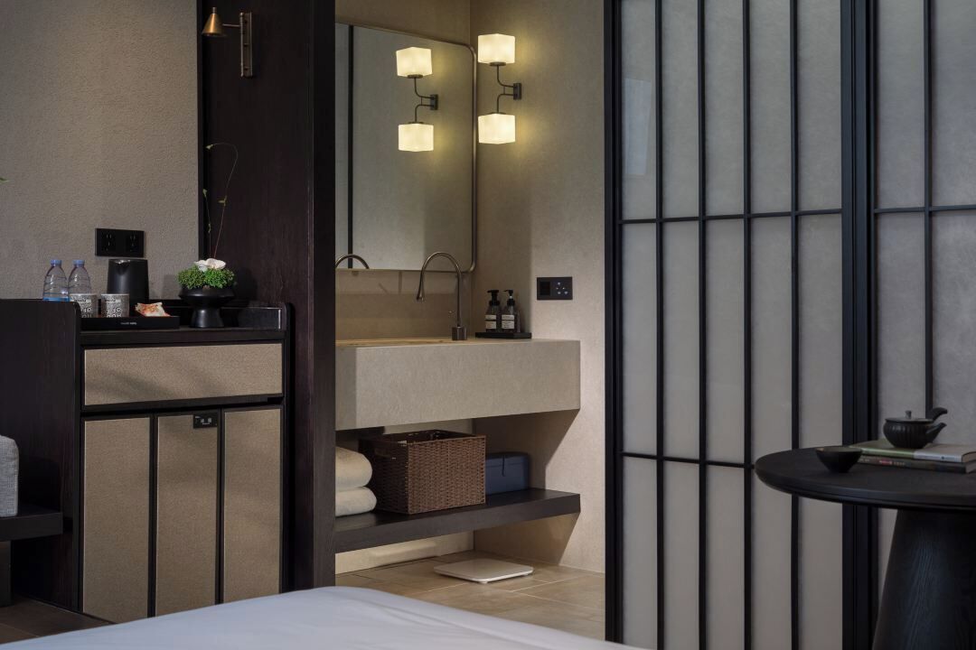 Une salle de bain moderne avec un grand miroir, un lavabo et une petite table sur laquelle se trouvent un livre et une théière.