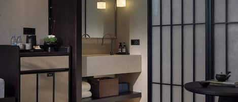 Une salle de bain moderne avec un grand miroir, un lavabo et une petite table sur laquelle se trouvent un livre et une théière.