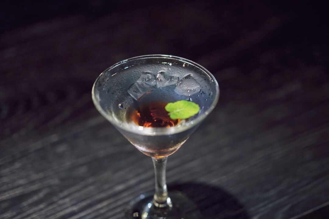 A martini glass with a mint leaf garnish on a dark wooden surface.