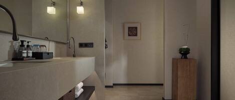 Une salle de bain moderne avec un grand miroir, deux appliques murales, un meuble-lavabo en bois et une petite plante en pot.