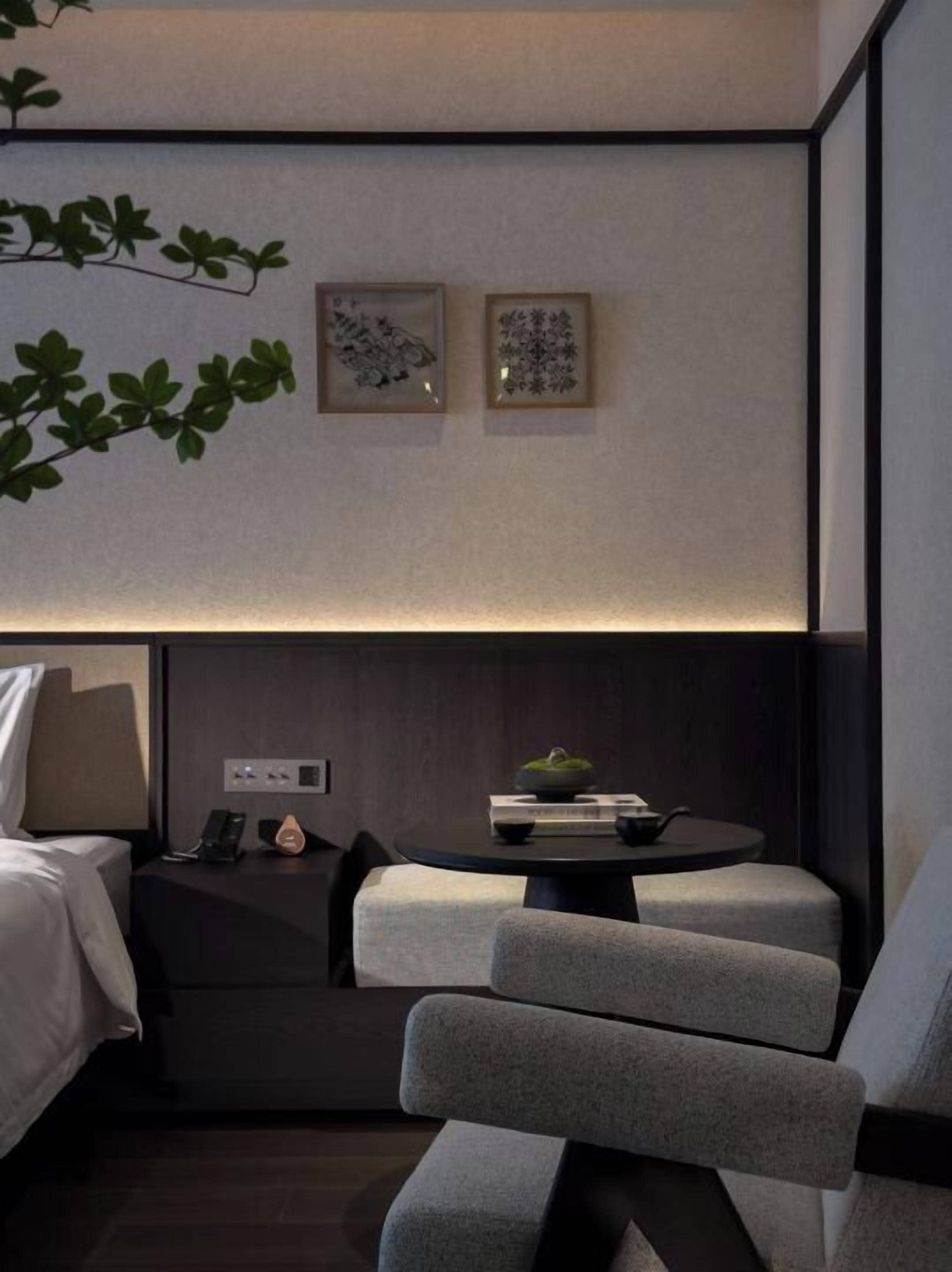 A modern hotel room with a bed, a seating area with a table, and two framed artworks on the wall.