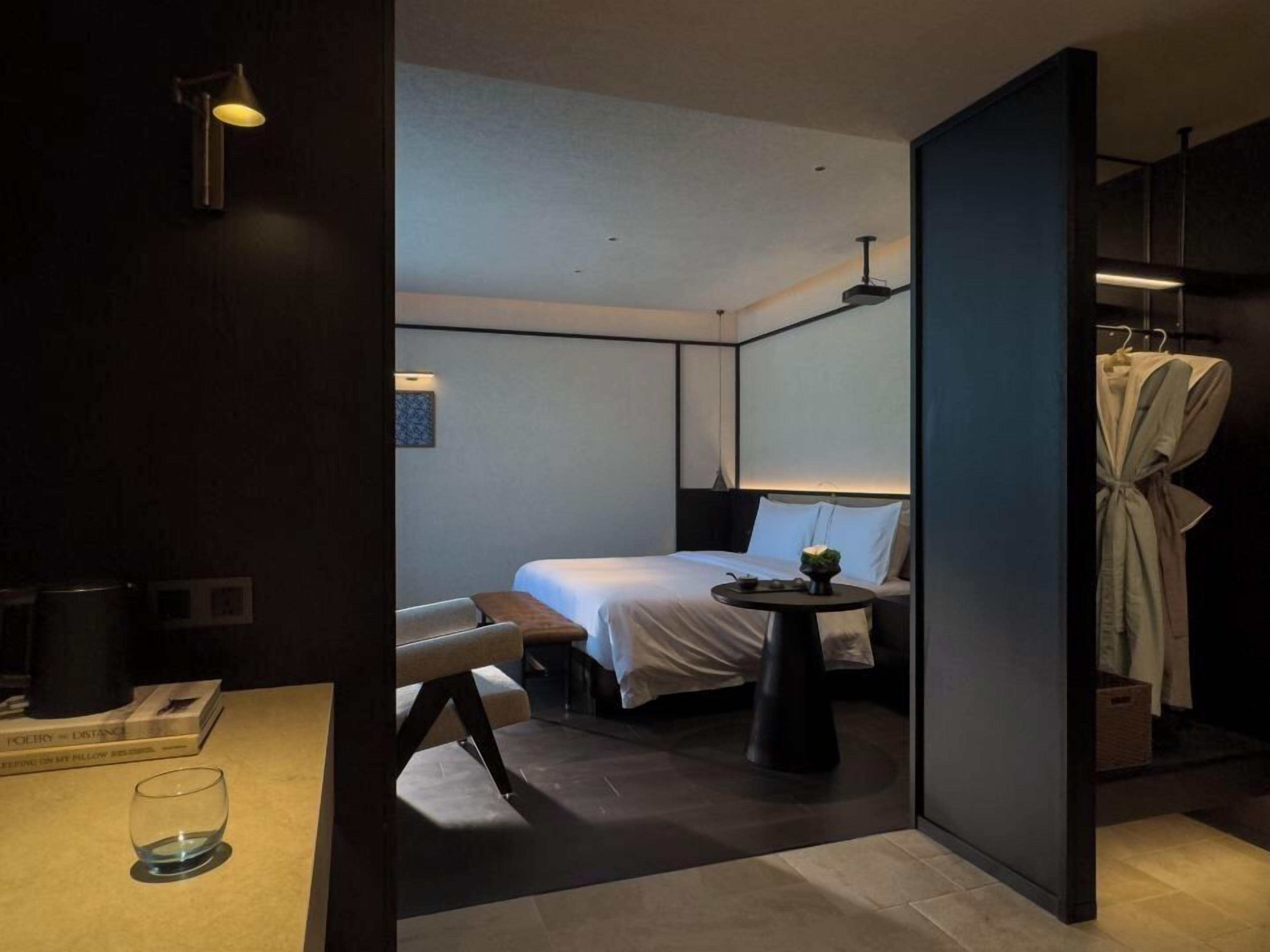 Een moderne hotelkamer met een bed, nachtkastje en een badjas hangend aan een rek.
