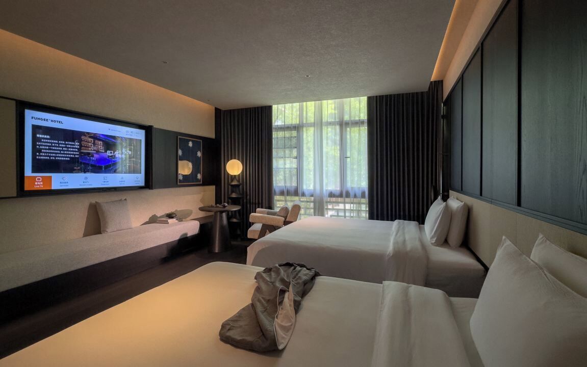Une chambre d’hôtel avec deux lits, un bureau, une chaise, une télévision et une grande fenêtre avec des rideaux.