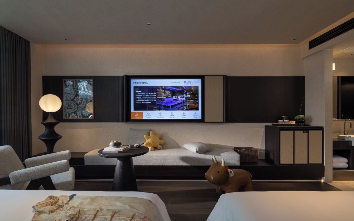 Une chambre d’hôtel moderne équipée d’un grand téléviseur à écran plat fixé au mur, d’un canapé, d’une petite table ronde et d’une statuette de vache décorative.