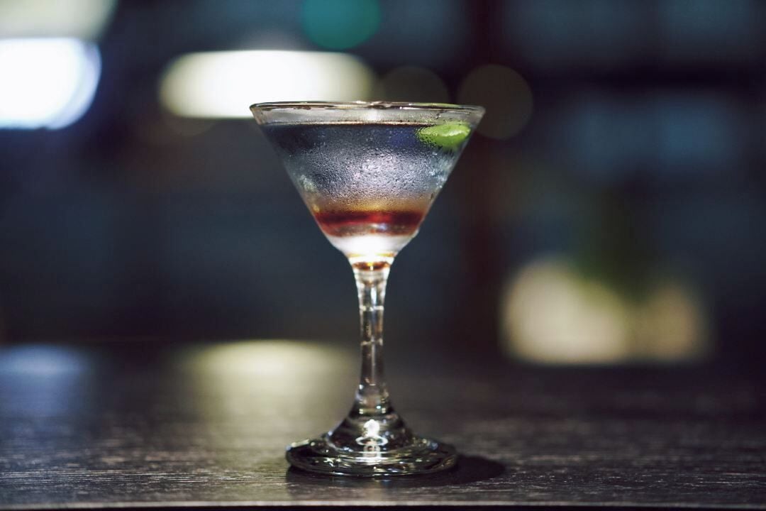 A martini glass on a dark surface with a blurred background.