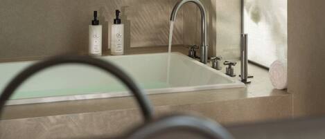 A modern bathroom with a bathtub, a faucet, and two bottles of lotion on the counter.