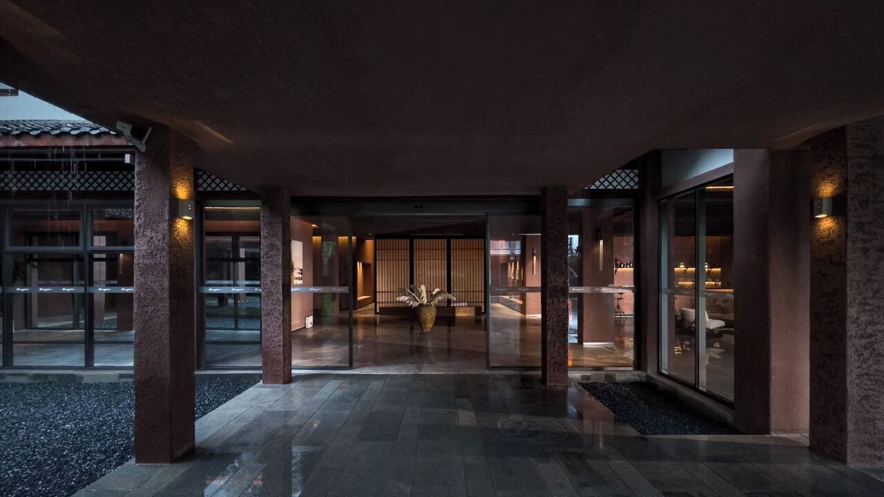 Un moderno vestíbulo de hotel con una entrada amplia, pilares grandes y un interior tradicional visible a través de puertas de vidrio.