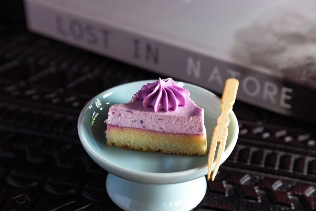 Eine Kuchenstück auf einem kleinen Teller mit einem Zahnstocher, platziert auf einem blauen Keramikteller.